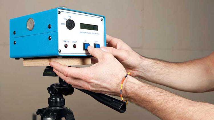 Man with a thin string bracelet pushing a button on a radon detector.